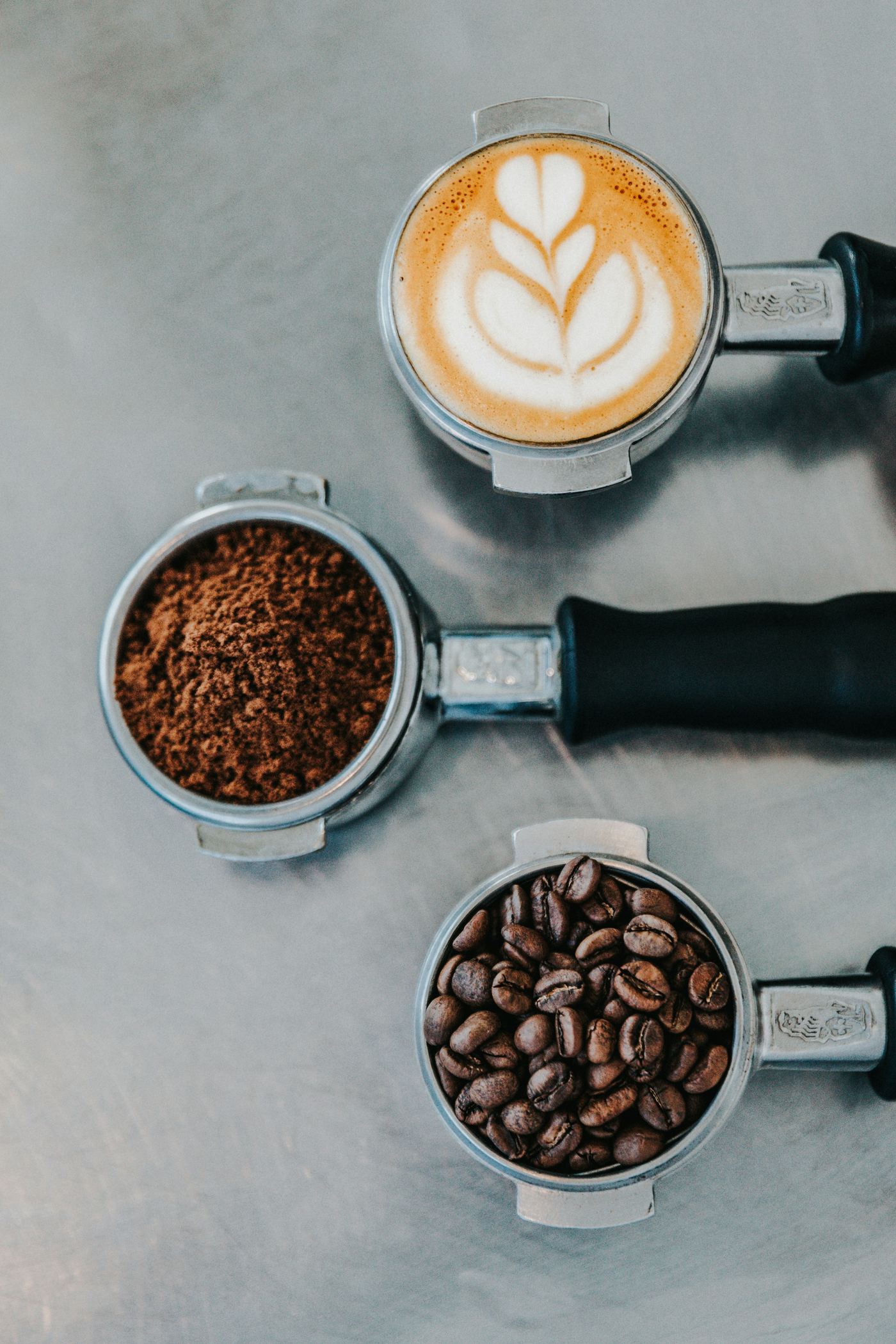 Espresso portafilters with whole beans, ground coffee, and a finished latte